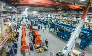 An aerial view of the assembly shop floor at Marine Travelift and Shuttlelift - there are orange and blue crane components in production.