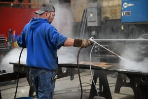 An ExacTech employee sprays water on a fresh weld on a large piece of structural steel