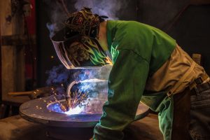 An ExacTech employee in protective welding gear welds a large round structural steel piece for a Marine Travelift crane